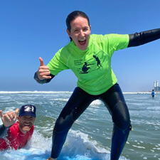 a first responder health care worker rides a wave with the assistance of a surf instructor in manhattan beach ca jmmf surf therapy